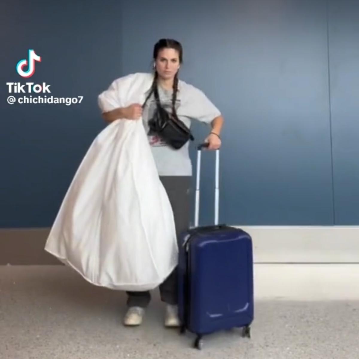 @chichidango7 walks through the airport with a wedding dress and suitcase.