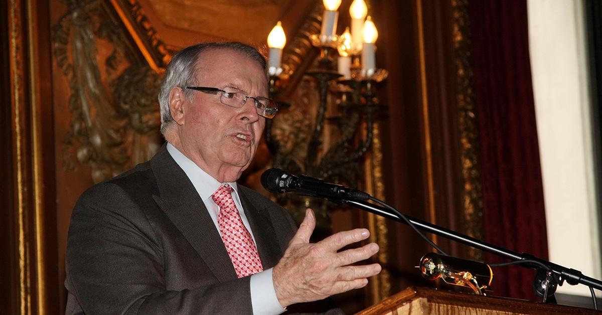 Charles Osgood speaking at a lectern in a suit and tie. 