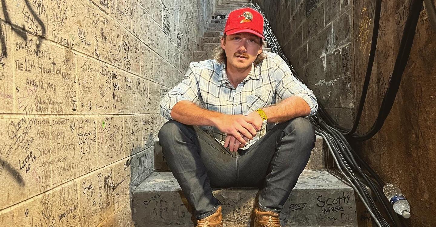 Morgan Wallen wears a red hat, sits on a staircase at Red Rocks Amphitheater in Morrison,Colorado.