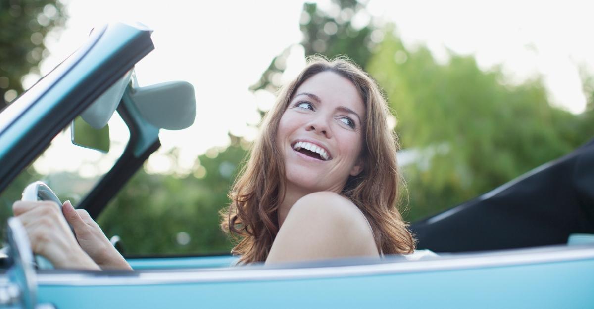 Woman happily driving in a convertible car - Stock Photo