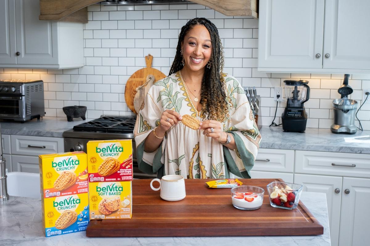 Tamera Mowry-Housley poses with belVita breakfast biscuits in a kitchen.