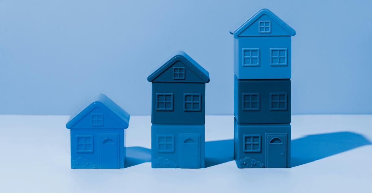 Thee blue toy houses of different heights stand next to each other against a blue backdrop.
