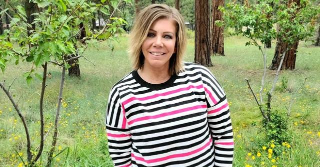 Meri Brown smiles and poses outside in a black, white, and pink LuLaRoe sweater.
