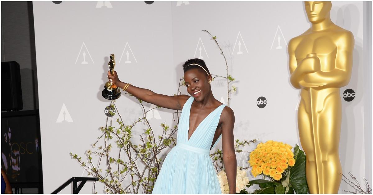 Lupita Nyong'o holding her Oscar and smiling.