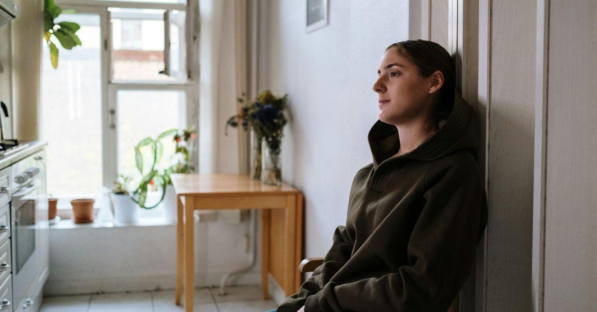 A woman sitting and staring in an apartment kitchen. 