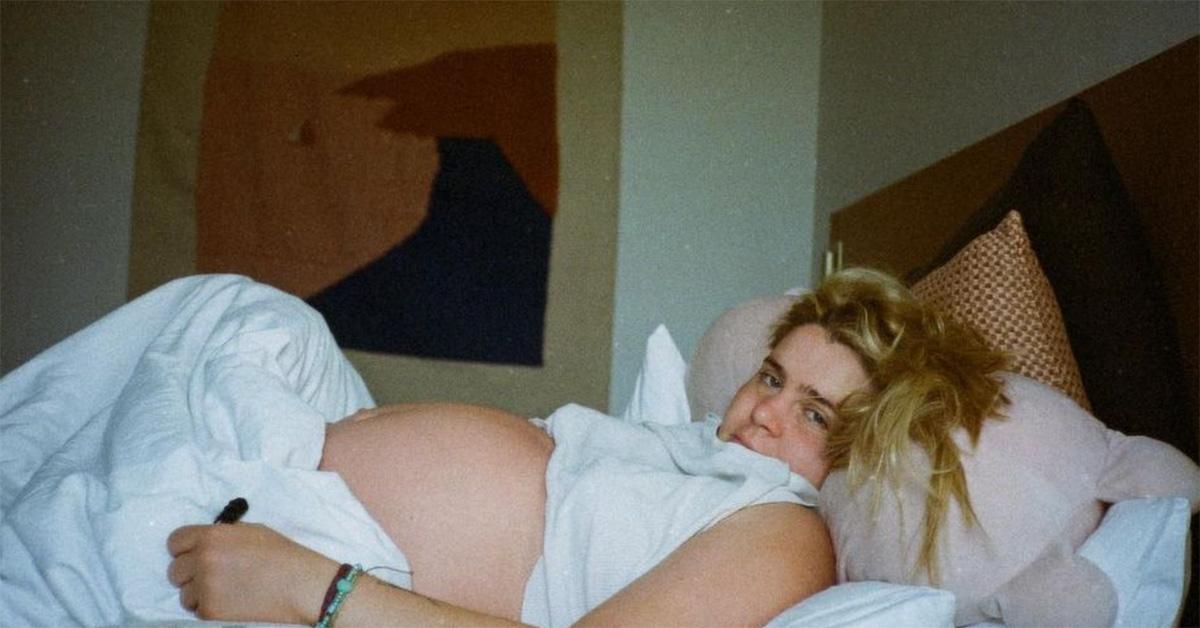 Mae Whitman laying in bed with a pregnant belly. 