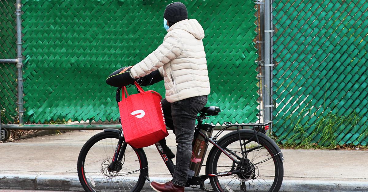 A person performing a DoorDash delivery on a bike