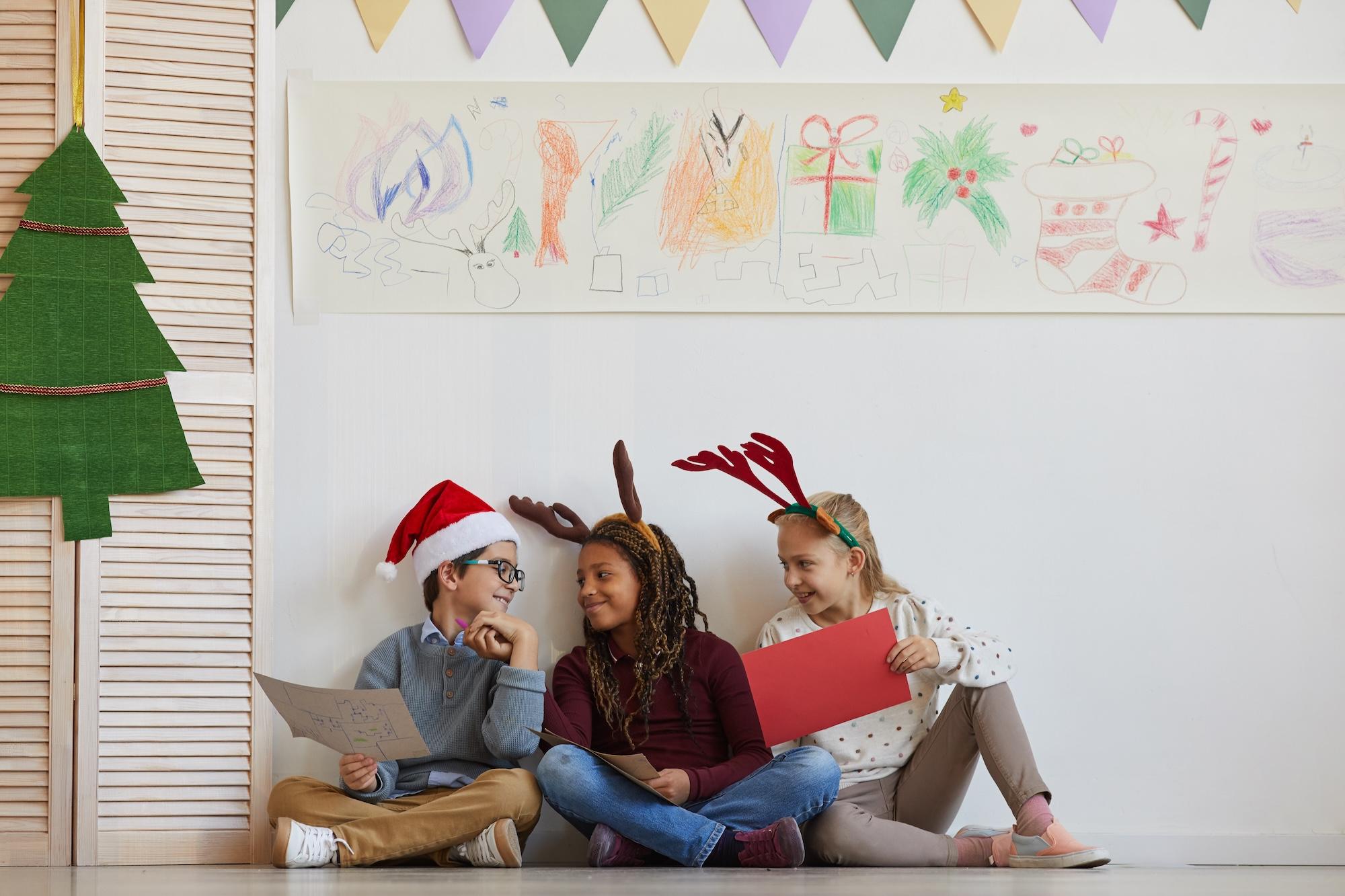Three kids sitting on the floor and holding pictures during a Christmas art class 