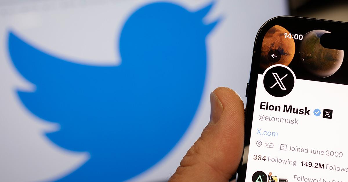 Twitter logo in the background with a hand holding a phone with Elon Musk's Twitter profile on it in the foreground. 