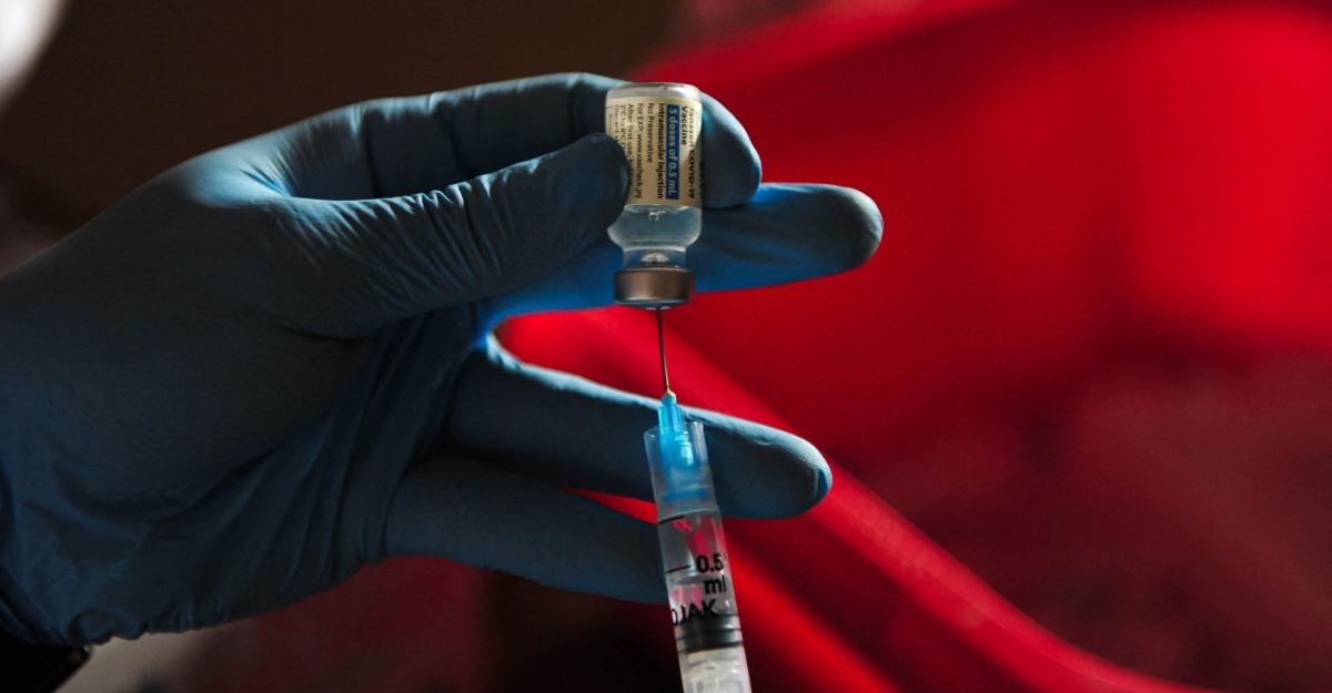 A gloved hand uses a syringe to administer the covid vaccine.