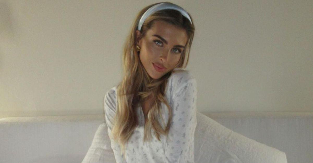 Paige Lorenze poses in her bed wearing white pajamas and a blue headband. 