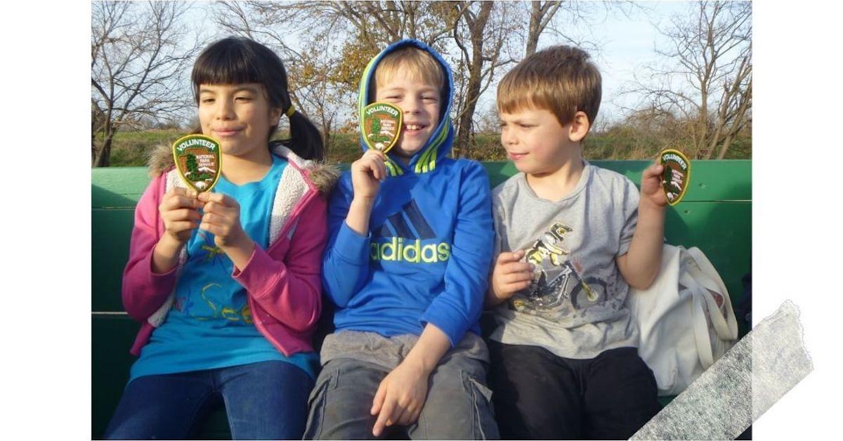 Three kids from Camp Fire look at their volunteer badges while seated on a bench