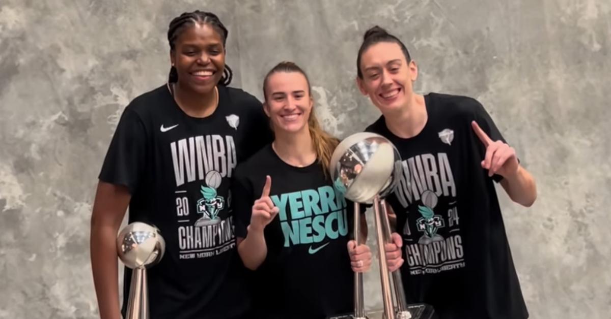 Jonquel Jones, Sabrina Ionescu, and Breanna Stewart taking photos after the Liberty won the 2024 WNBA Championship.