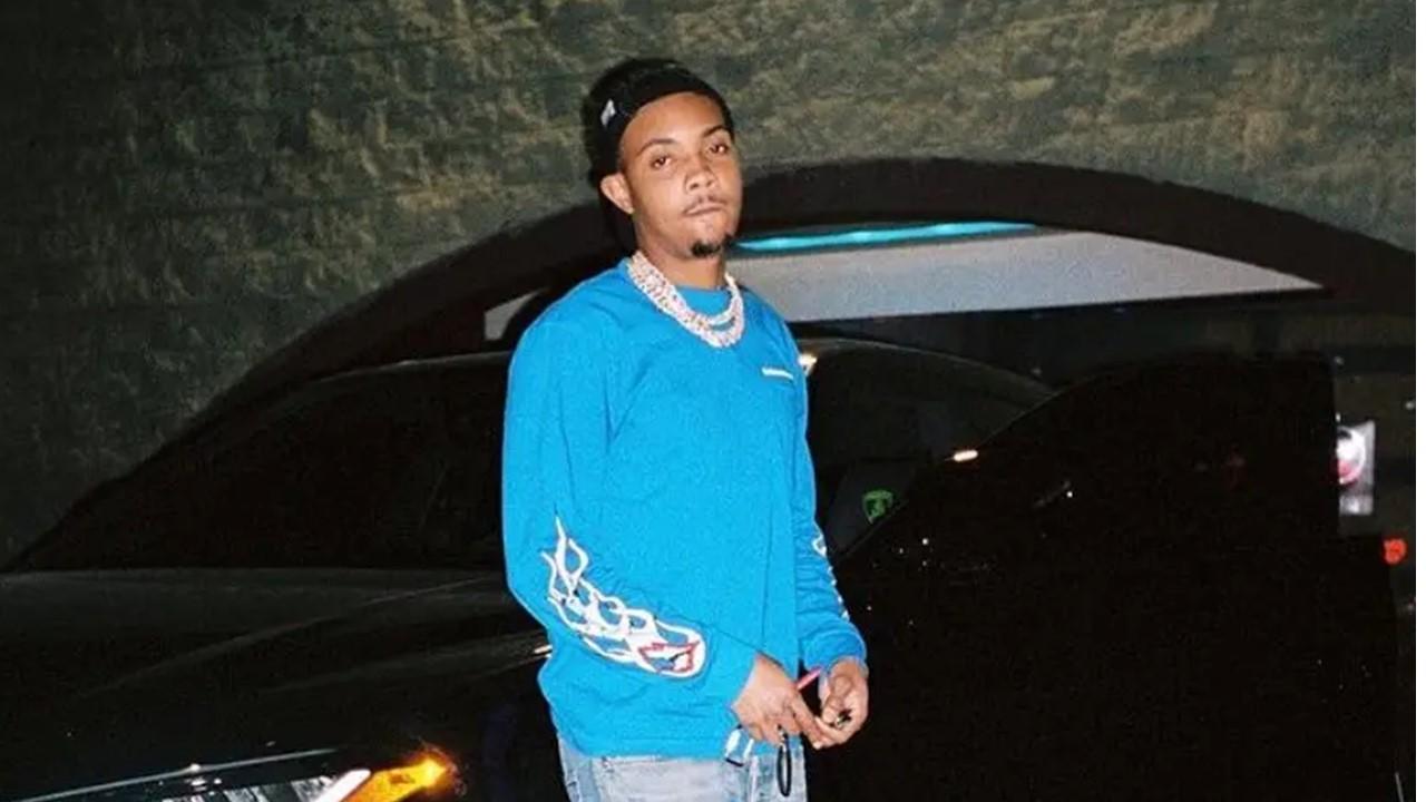 G Herbo wearing a blue long-sleeved shirt and jeans next to a car.