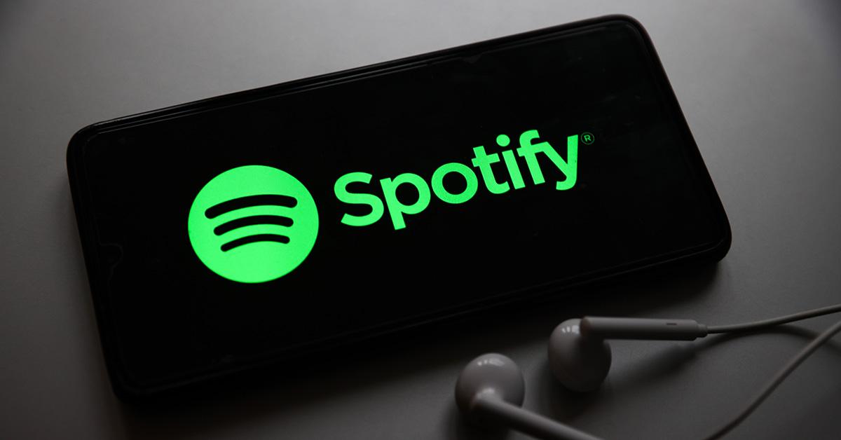 A Spotify logo on a phone with headphones sitting next to it. 