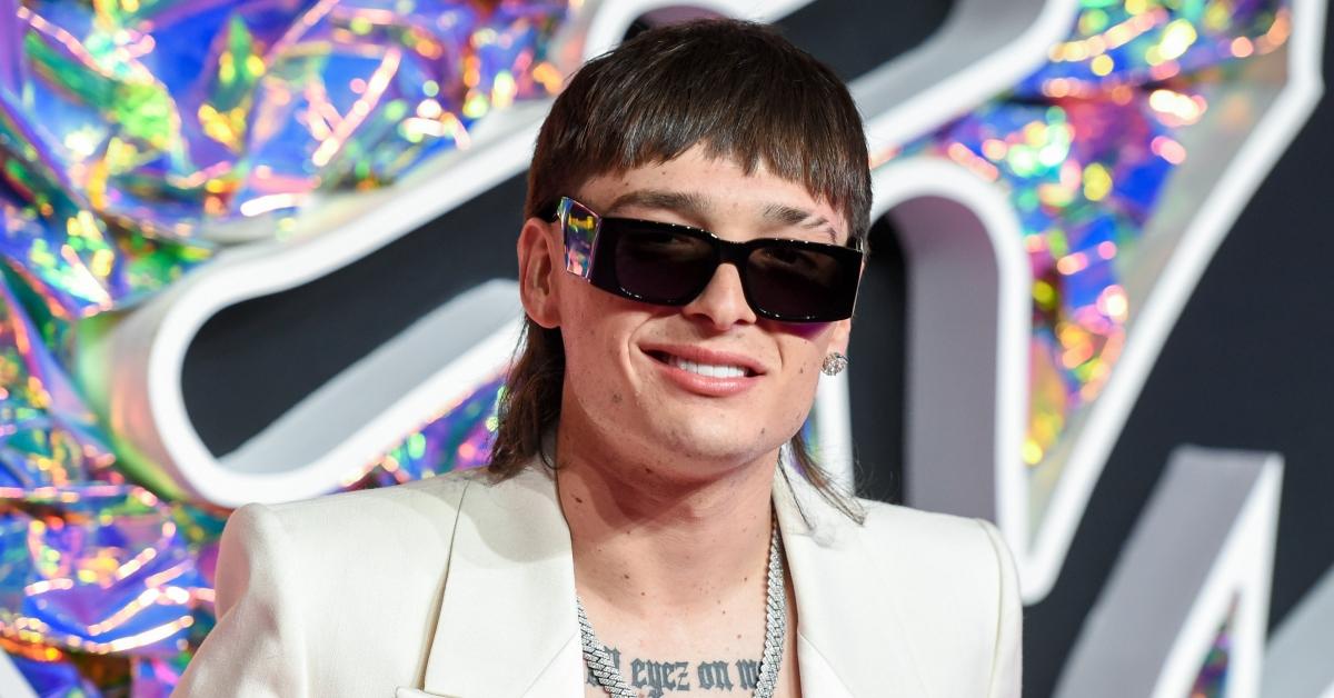 Peso Pluma on the red carpet of the 2023 MTV VMAs wearing a white tux and sunglasses.