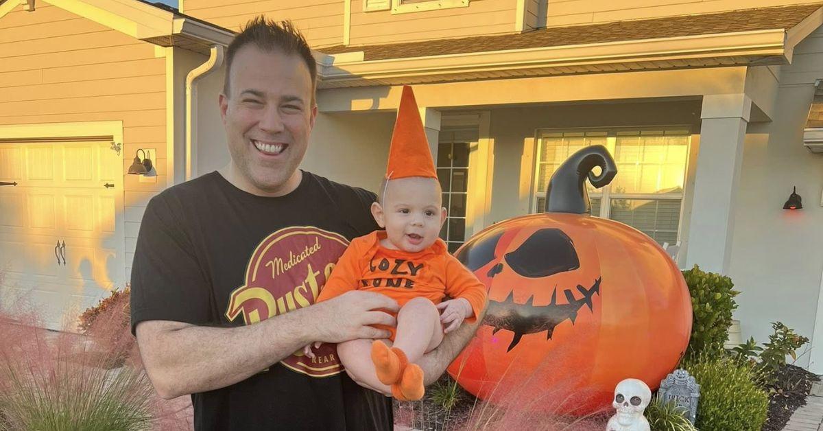 Matt Devitt holding a baby dressed in orange on his lawn.