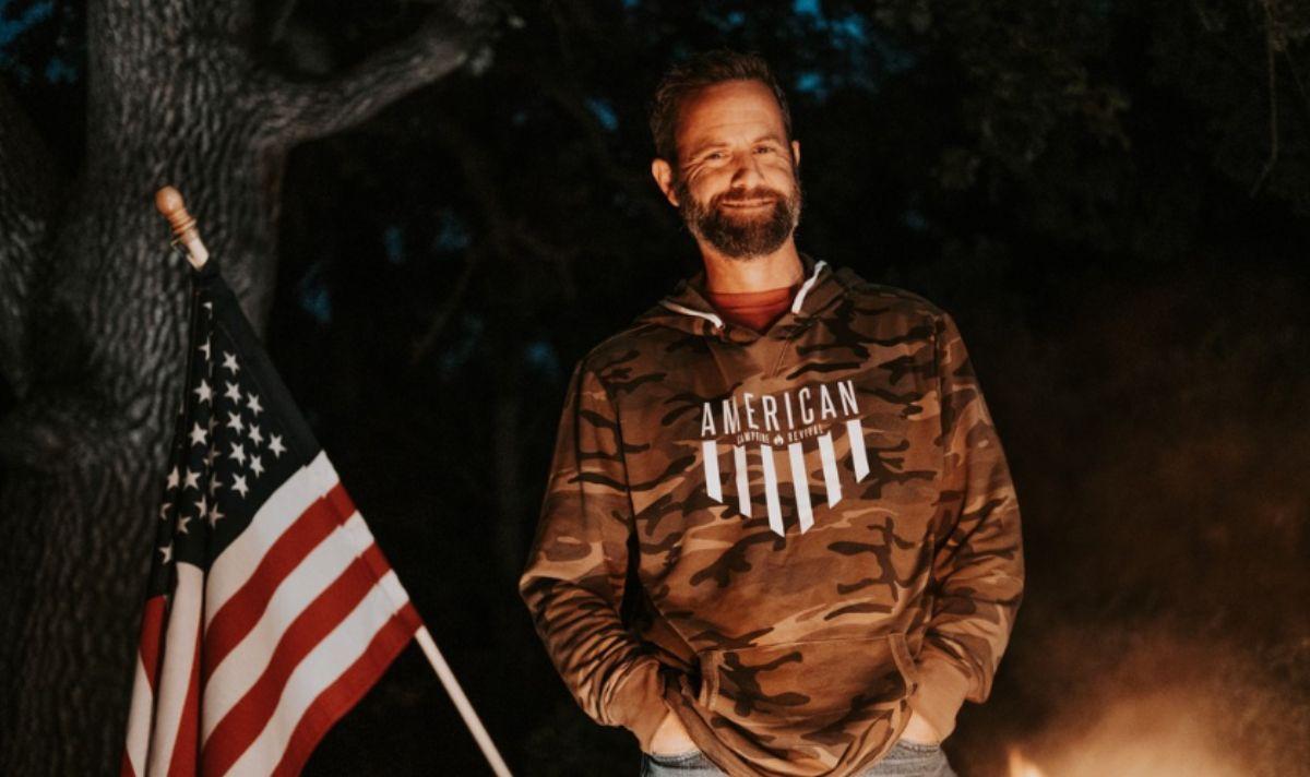 Kirk Cameron poses in a camo sweatshirt next to an American flag