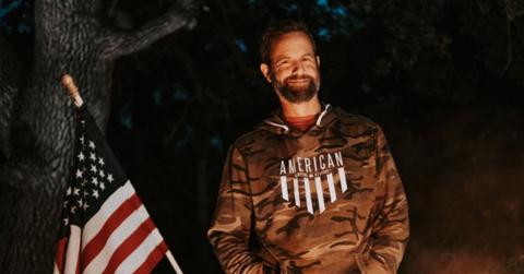 Kirk Cameron poses in a camo sweatshirt next to an American flag