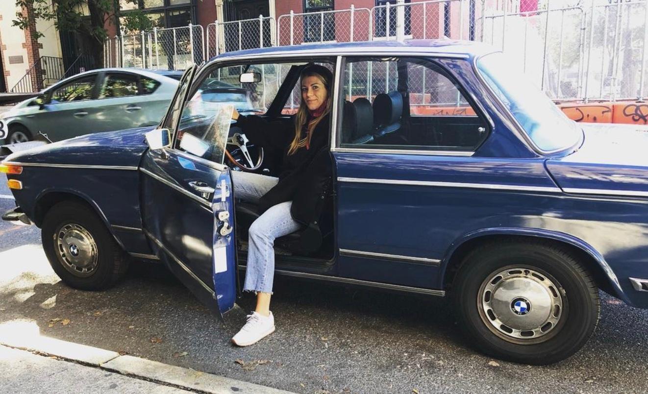 Still shot of Mae sitting in a vintage vehicle