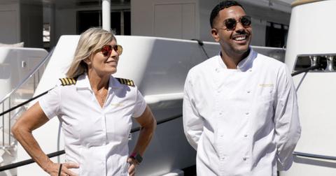 Captain Sandy Yawn and chef Jono Shillingford standing on the Mustique looking off camera and smiling, both wearing sunglasses.
