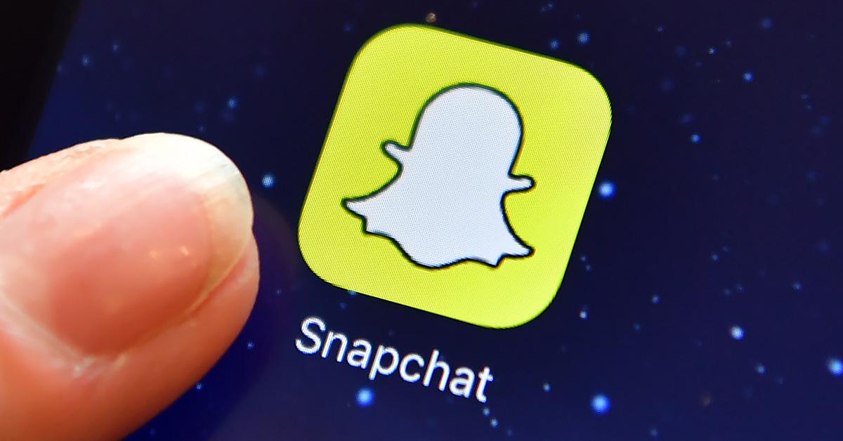A snapchat logo on a phone screen with a finger. 