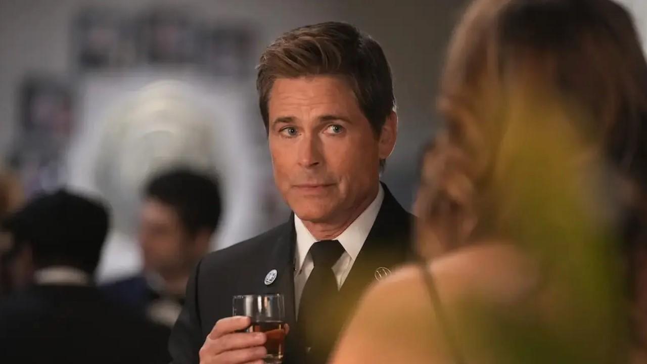 Owen in a black suit, holding a drink, and talking to Kendra.