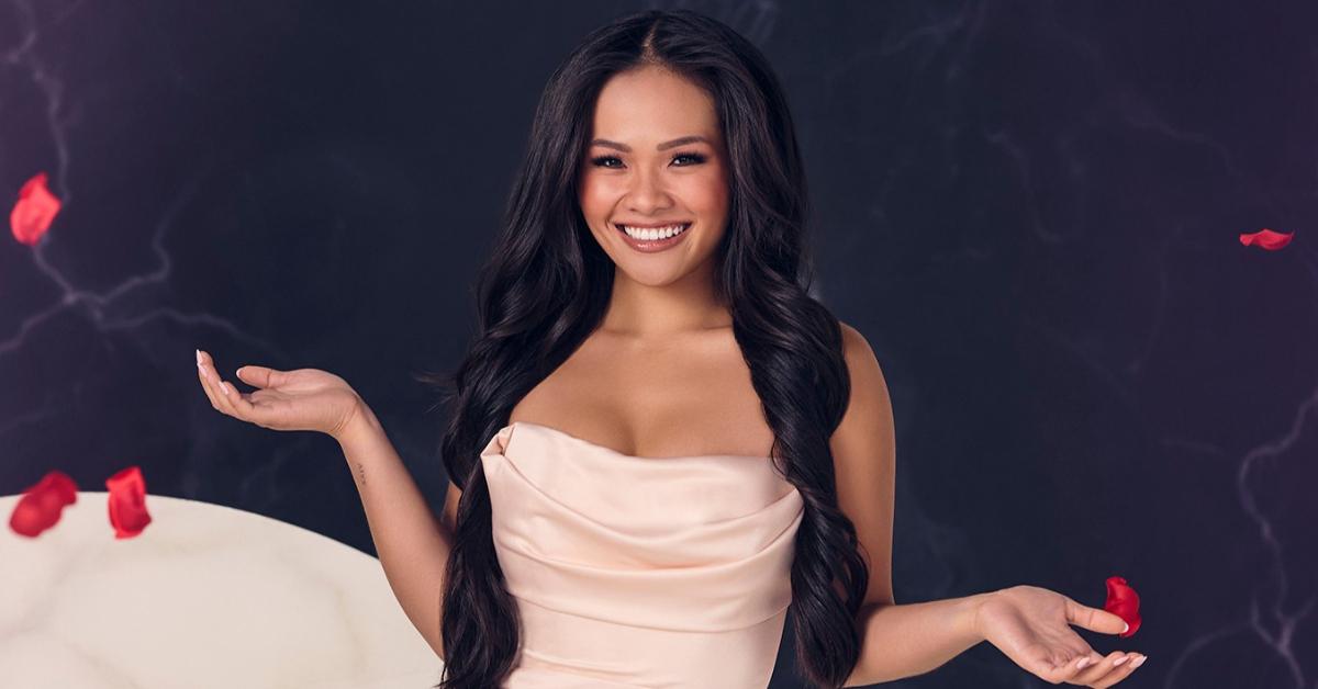 Jenn Tran smiles and poses in a strapless light pink gown while red rose petals float in the air around her.