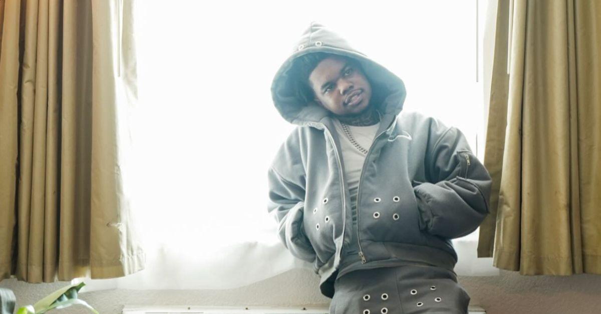 Lil Poppa leaning against a window in a motel room. 