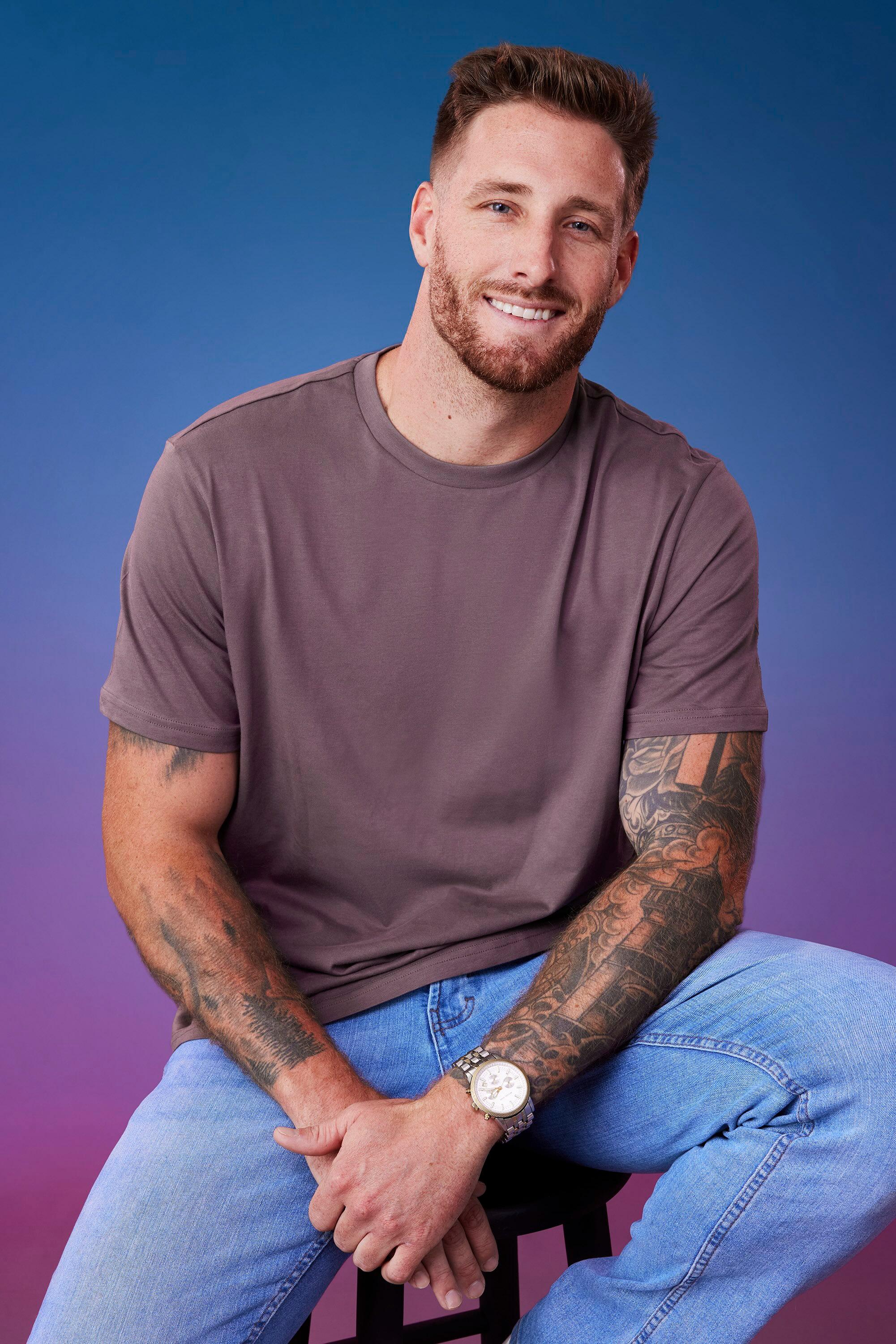 Sam M. poses in front of a blue-purple ombré background for his official 'The Bachelorette' Season 21 portrait.