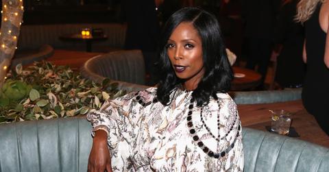 Tasha Smith wearing a dress sitting on a blue loveseat.