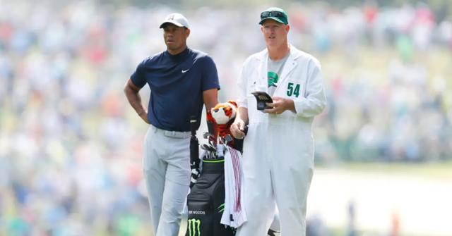 Tiger Woods and his caddy wearing a white jumpsuit on the golf course.