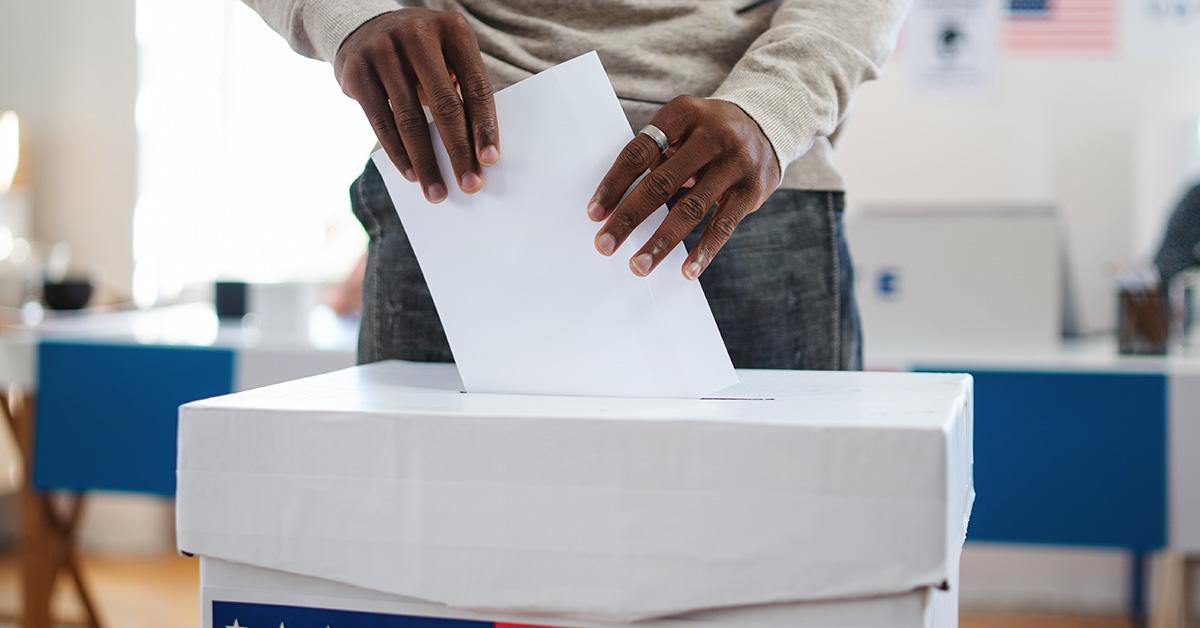 A person submitting a ballot into a ballot box. 