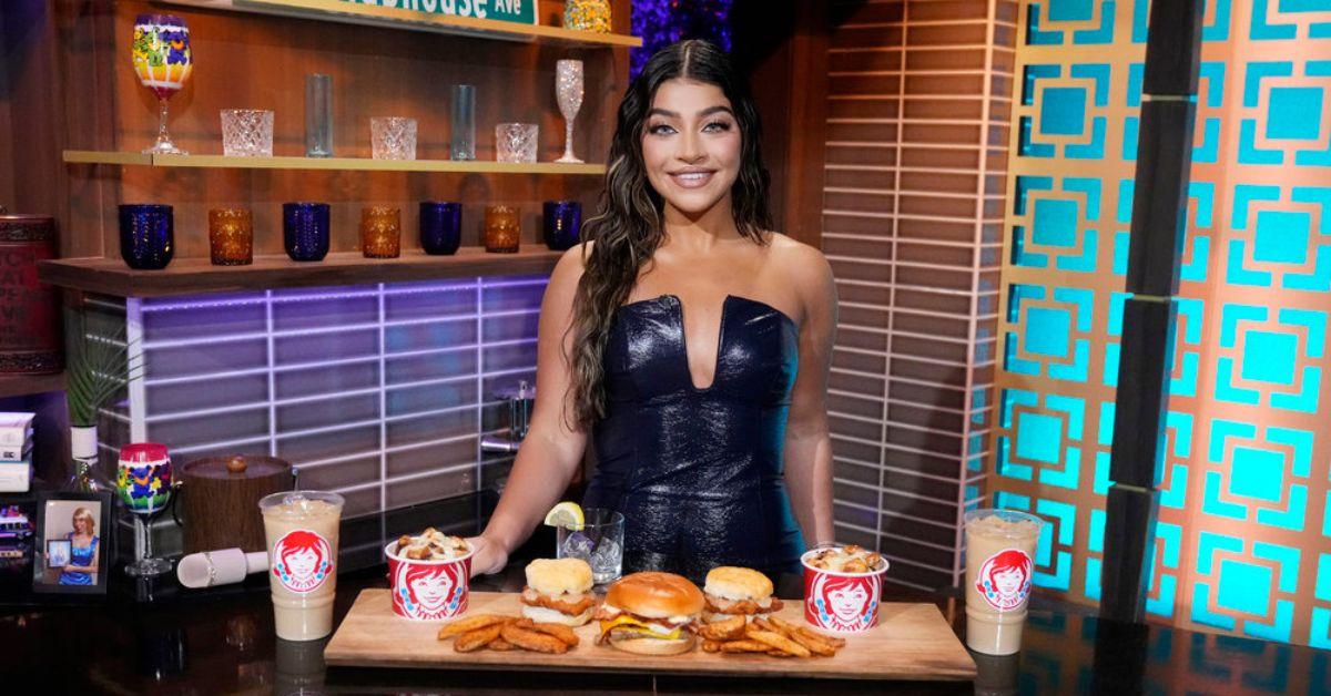 Gia Giudice posing for photo behind a spread of food from Wendy's on 'WWHL'