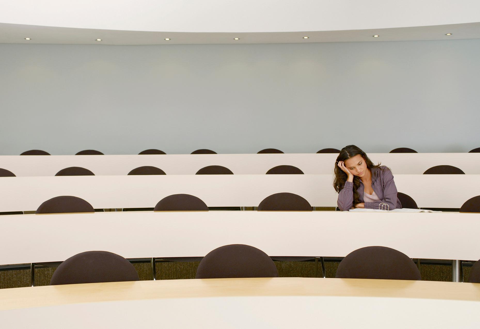 A photo of a student, stressed, taking an exam in an empty lecture room. 