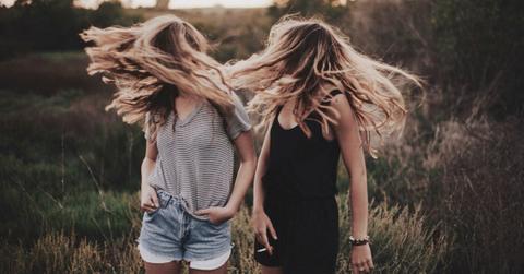Two girls flip their hair while standing in a field