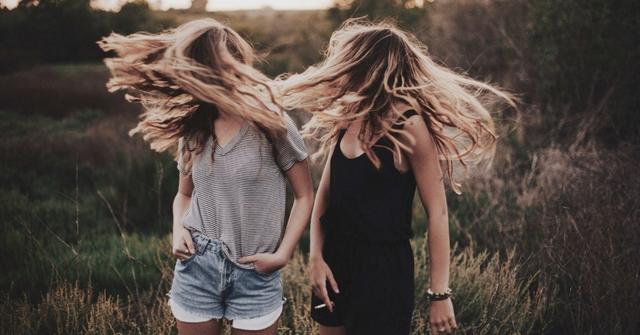 Two girls flip their hair while standing in a field