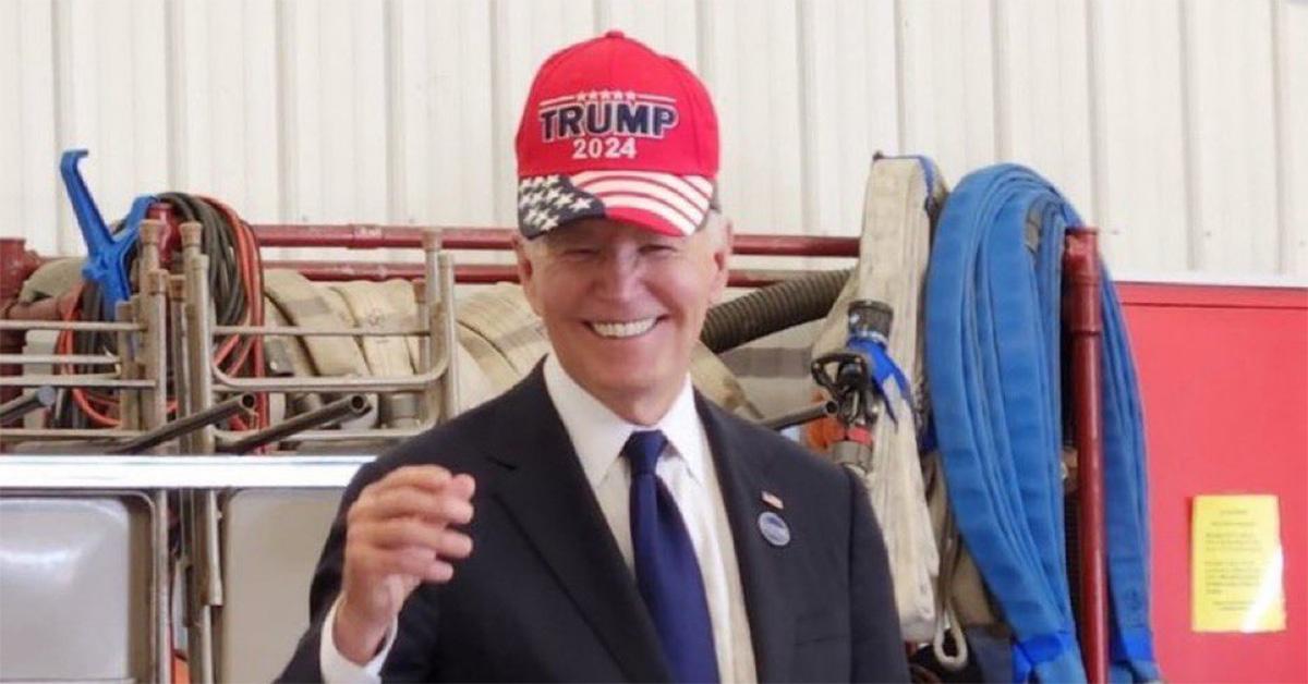 Joe Biden smiles while wearing a Trump hat. 