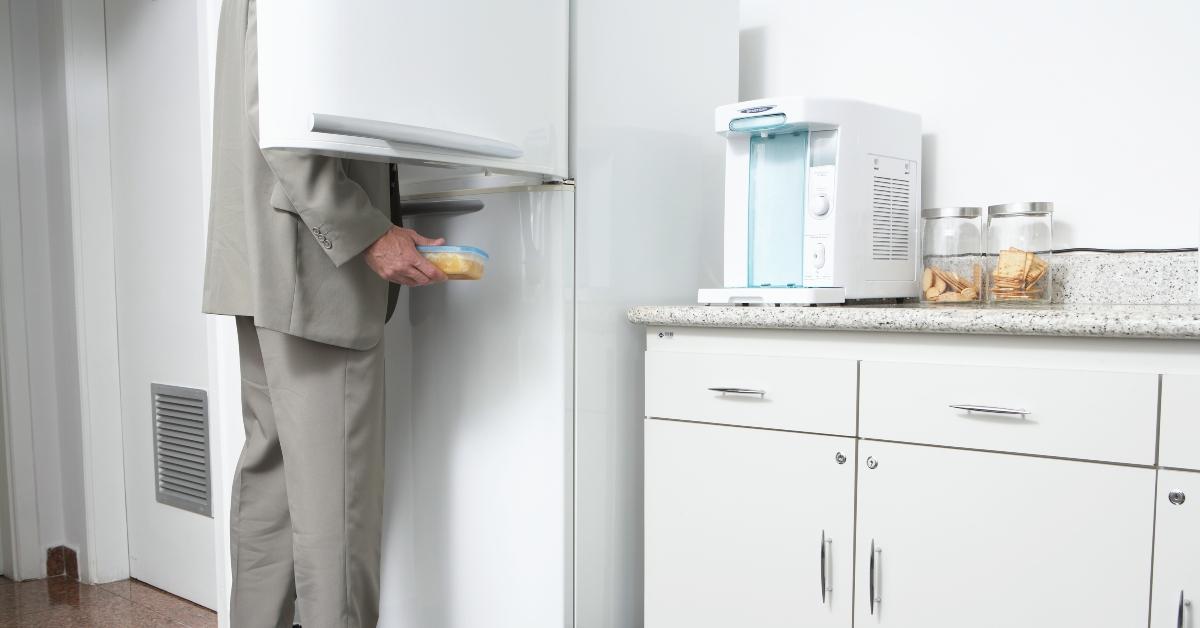 Man removing food from refrigerator in office kitchen, low section - stock photo