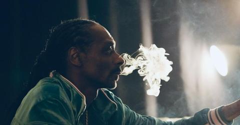 Snoop Dogg wearing a green jacket and smoking weed