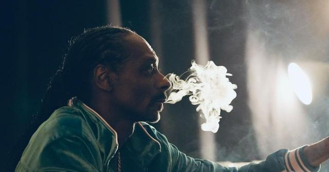 Snoop Dogg wearing a green jacket and smoking weed