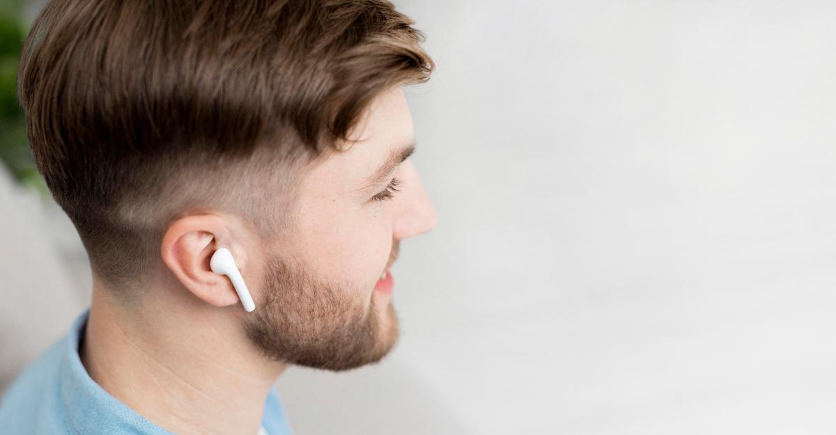 Man in blue shirt smiles and uses an AirPod