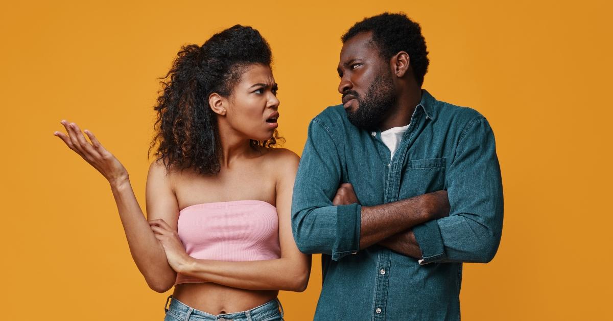Young black couple gesturing and having conflict while standing against yellow background