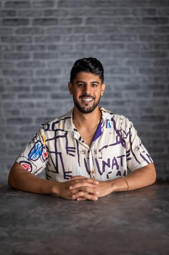 Neesh wears a paint-splattered button up, smiling for his official portrait for Season 2 of 'The Mole.'