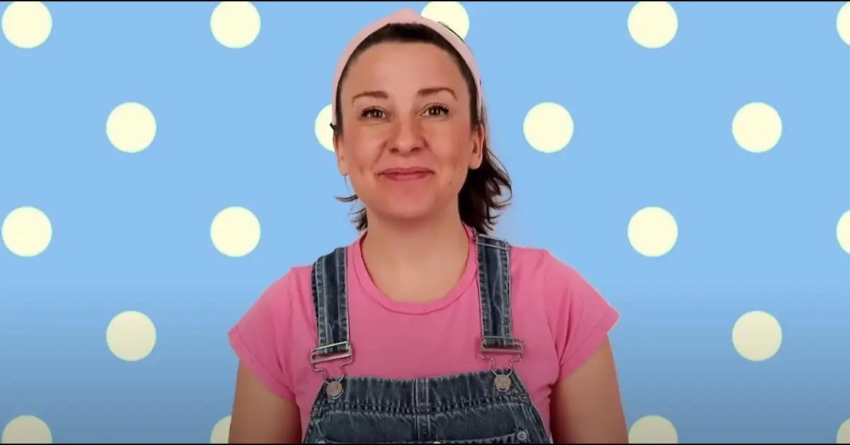 Ms. Rachel wearing her trademark out, blue overalls and a pink t-shirt.