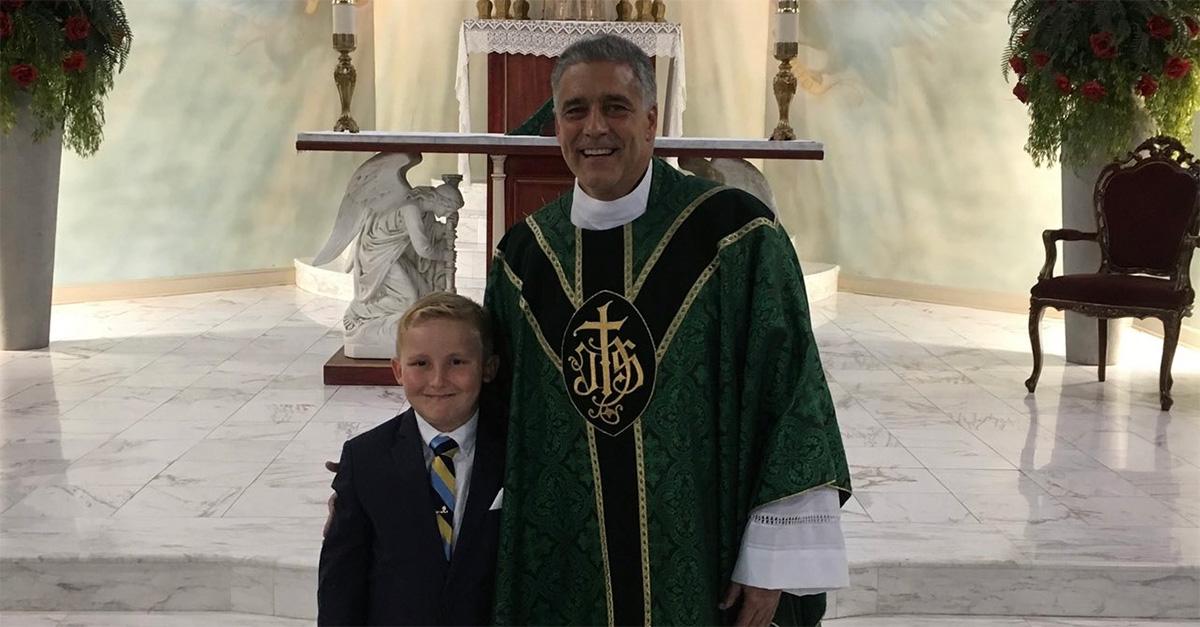 Father Mark Beard in robes posing with a child in a suit and tie. 