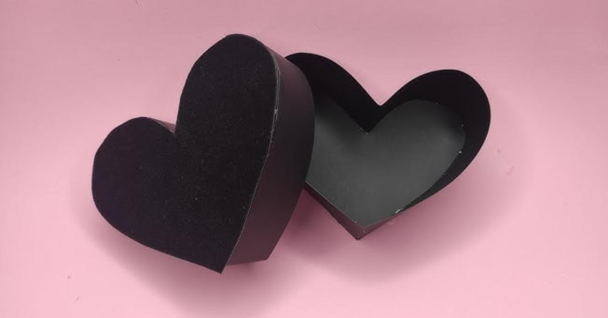 Black heart-shaped gift box placed on top of a light pink table.