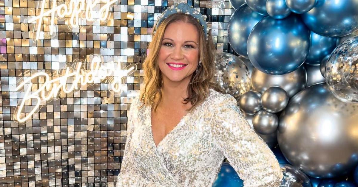 Danielle Busby smiles and poses for her 40th birthday in a sparkly silver v-neck long-sleeve dress.