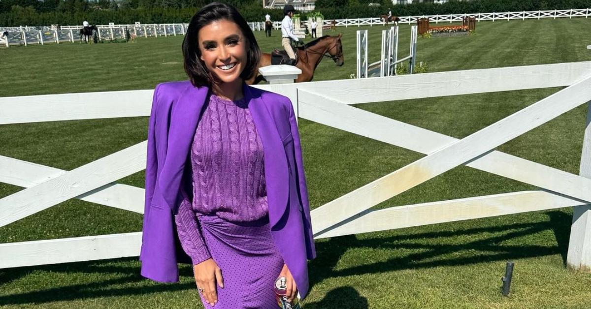 Bronwyn Newport stands in front of horses on a pasture in a purple outfit