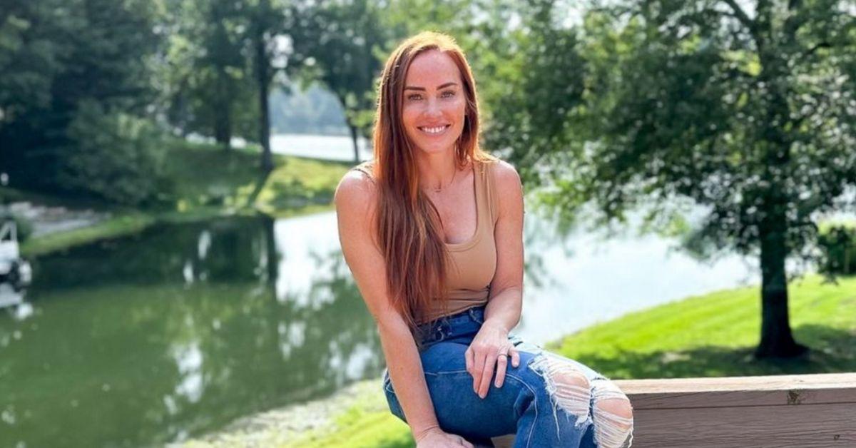 Mina Starsiak Hawk sits on a wooden deck, smiling in front of a river